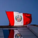 National Peruvian flag waving prominently against a clear blue sky, reflecting on a building.